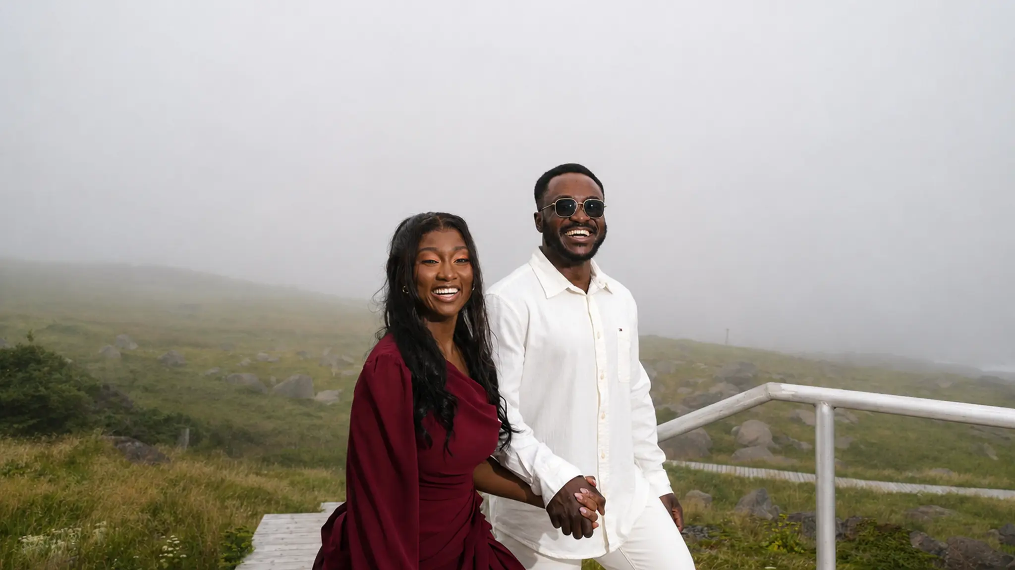 Kingsford and Perla smiling and holding hands at a misty coastal lookout.